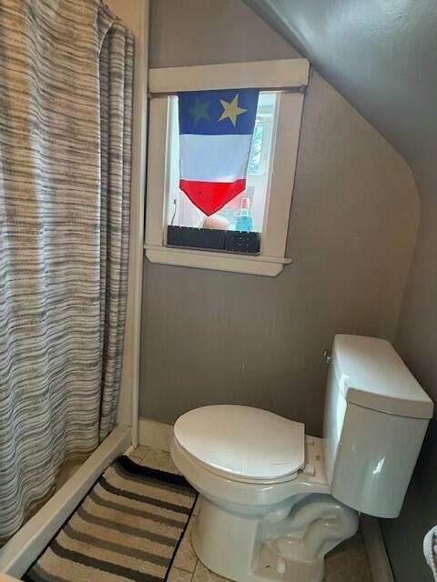 bathroom with tile patterned floors, vaulted ceiling, toilet, and curtained shower