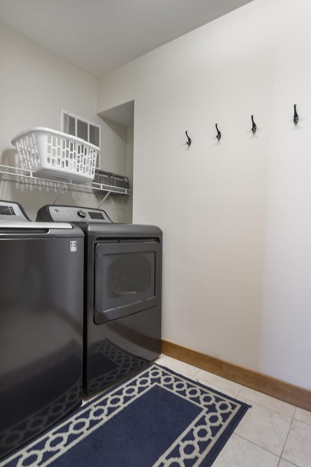 clothes washing area featuring washing machine and dryer, light tile patterned flooring, and baseboards