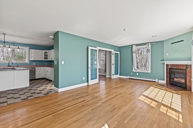 unfurnished living room featuring a fireplace, a sink, baseboards, a baseboard heating unit, and light wood-style floors