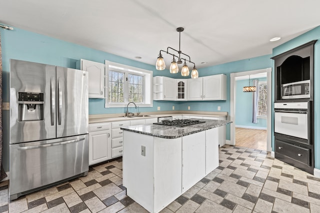 kitchen with a center island, white cabinetry, a sink, appliances with stainless steel finishes, and decorative light fixtures