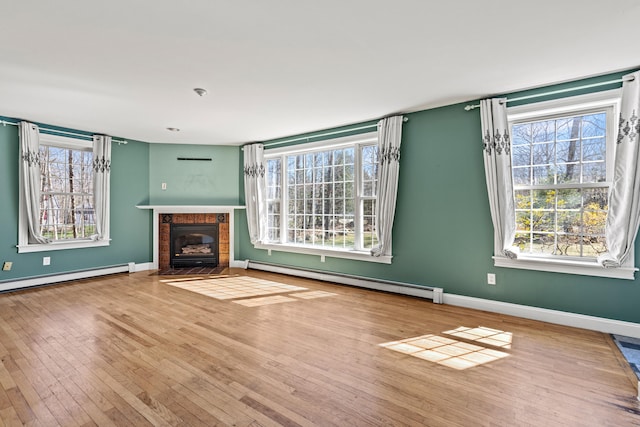 unfurnished living room featuring a healthy amount of sunlight, a baseboard heating unit, and hardwood / wood-style flooring