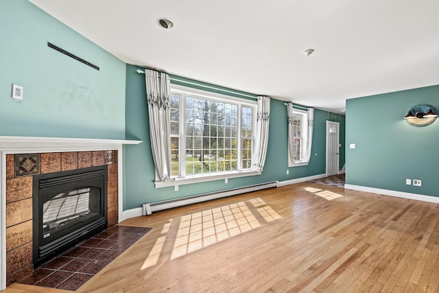 unfurnished living room featuring baseboards, baseboard heating, hardwood / wood-style flooring, and a tile fireplace