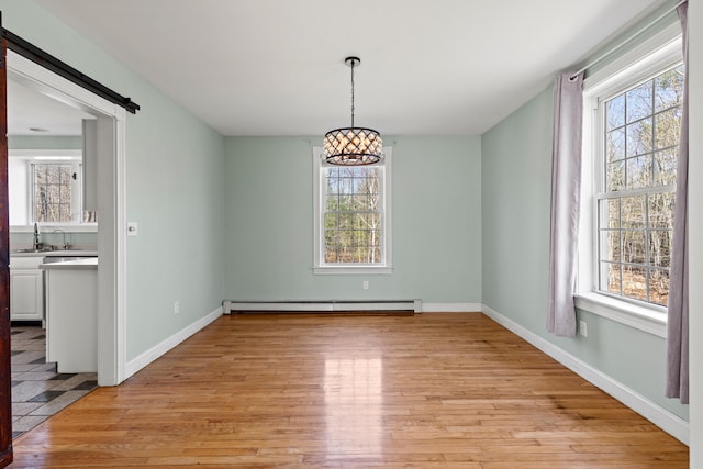 unfurnished dining area with a barn door, baseboard heating, light wood-style flooring, and a notable chandelier