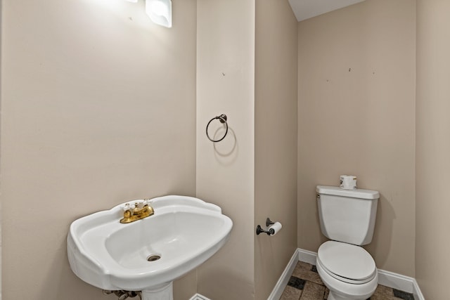 half bath with toilet, baseboards, and a sink