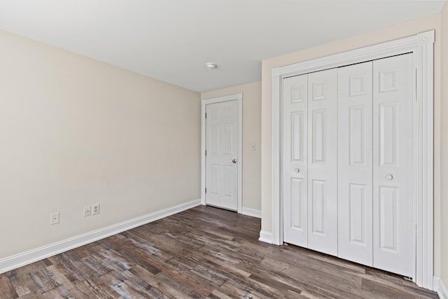 unfurnished bedroom featuring baseboards, dark wood-style floors, and a closet
