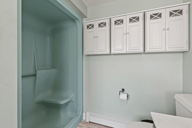 full bath with baseboard heating, wood finished floors, a walk in shower, vanity, and toilet
