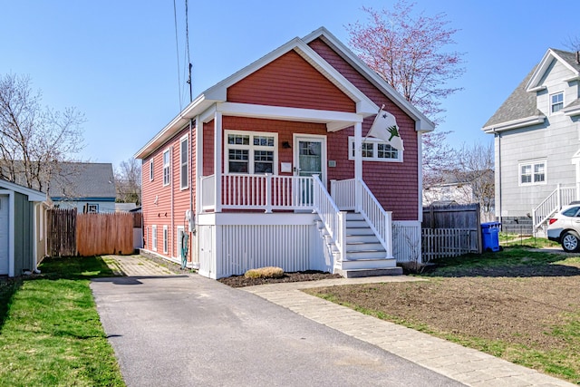 bungalow-style home featuring covered porch, fence, driveway, and stairs