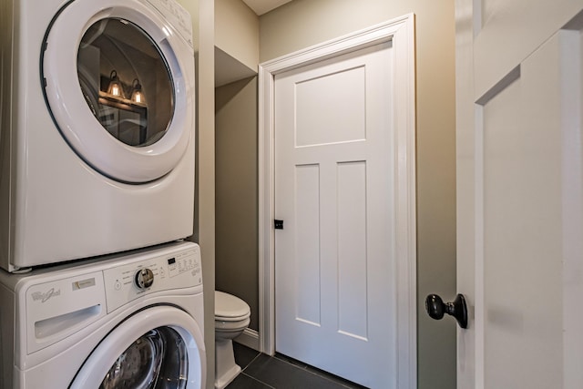clothes washing area with dark tile patterned flooring, stacked washer and clothes dryer, and laundry area