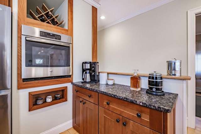 kitchen featuring crown molding, recessed lighting, dark stone counters, brown cabinets, and appliances with stainless steel finishes