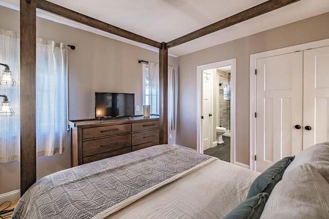 bedroom with baseboards, ensuite bath, a closet, and beamed ceiling