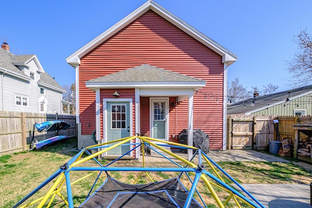 rear view of house with a fenced backyard, a yard, and roof with shingles