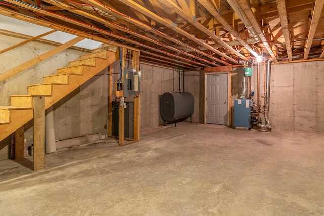 unfinished below grade area featuring a heating unit, heating fuel, electric panel, and stairway