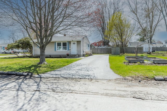 view of front of home featuring fence, aphalt driveway, a garden, and a front yard