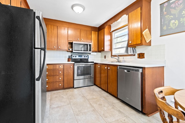 kitchen with backsplash, stainless steel appliances, brown cabinetry, and a sink