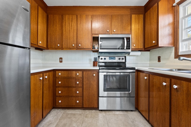 kitchen with light countertops, stainless steel appliances, brown cabinetry, and backsplash