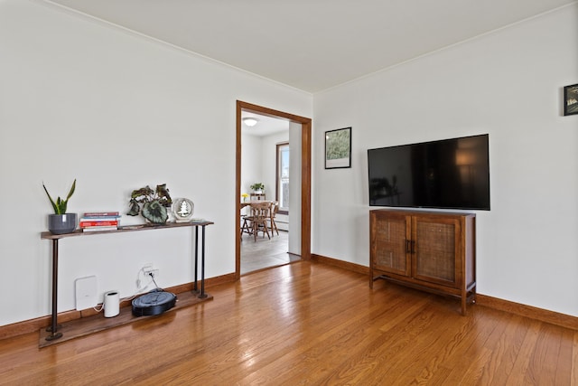 living room featuring wood-type flooring, baseboards, and crown molding
