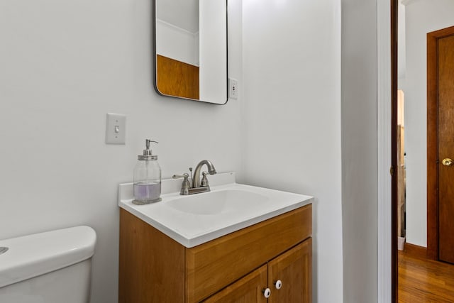 half bathroom with vanity, wood finished floors, and toilet