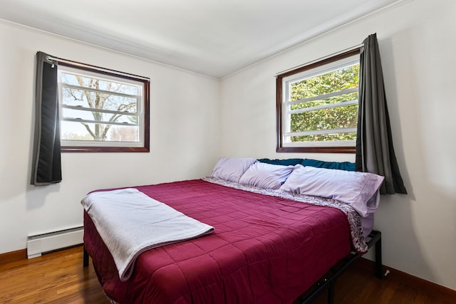 bedroom with baseboards, ornamental molding, baseboard heating, and wood finished floors