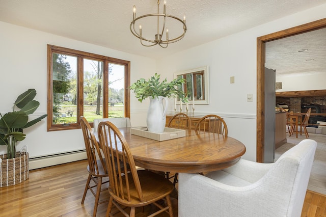 dining space featuring an inviting chandelier, a textured ceiling, light wood-style floors, and baseboard heating