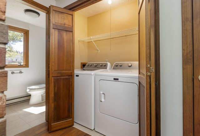 clothes washing area with laundry area, a textured ceiling, washing machine and clothes dryer, light wood-type flooring, and a baseboard radiator