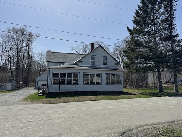 view of front facade with a garage, a chimney, and gravel driveway