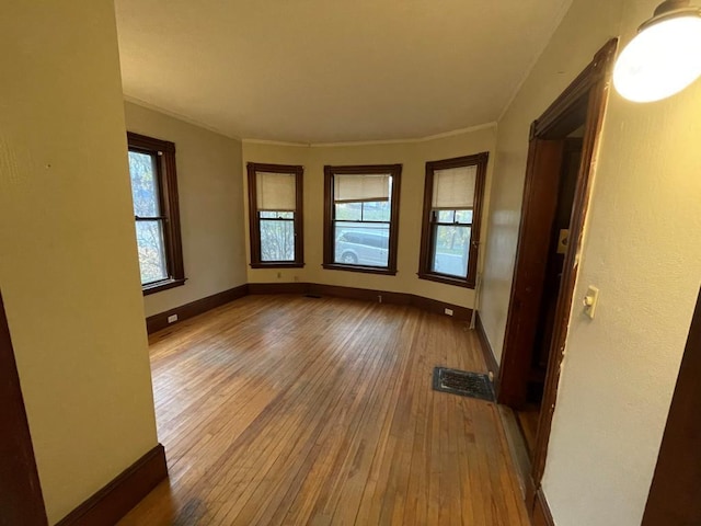 empty room featuring crown molding, baseboards, and hardwood / wood-style floors
