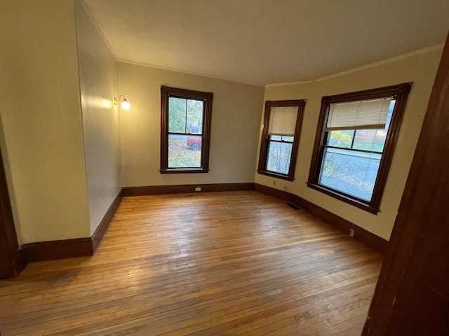 unfurnished room featuring crown molding, baseboards, a healthy amount of sunlight, and wood-type flooring