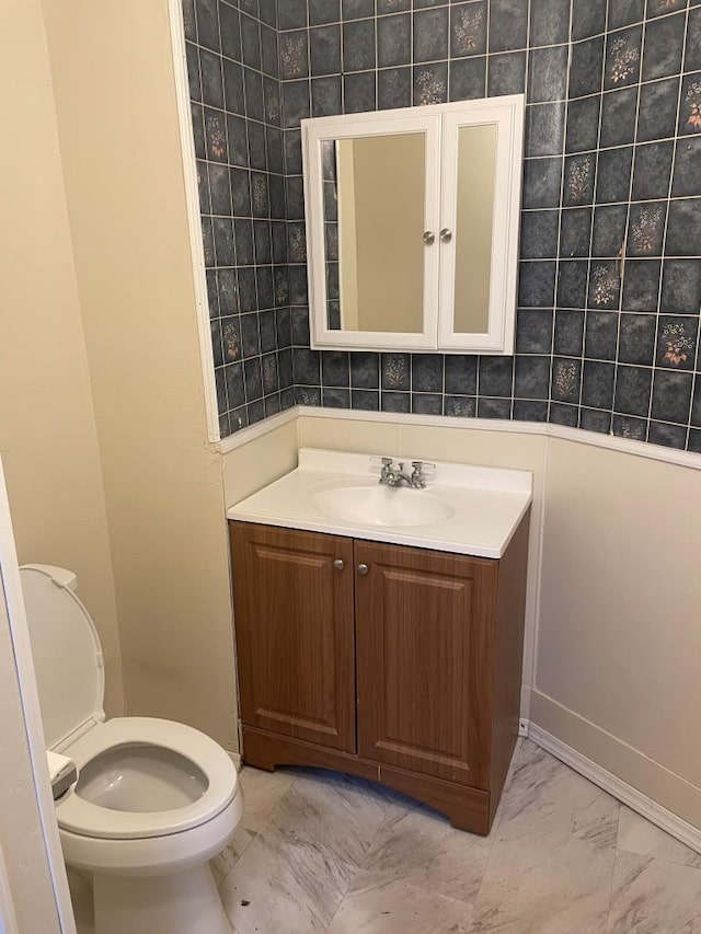 half bathroom with vanity, marble finish floor, and toilet