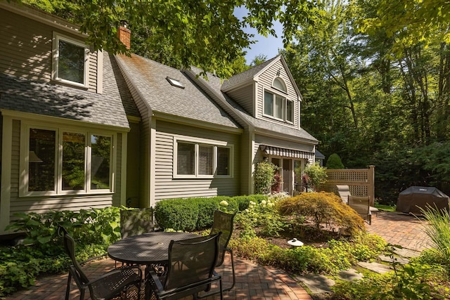 back of house with a patio, a chimney, outdoor dining area, and roof with shingles