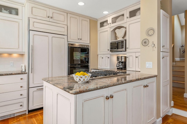 kitchen with appliances with stainless steel finishes, stone countertops, a peninsula, glass insert cabinets, and recessed lighting