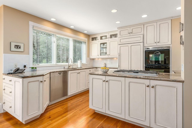 kitchen featuring glass insert cabinets, tasteful backsplash, a sink, light wood finished floors, and appliances with stainless steel finishes