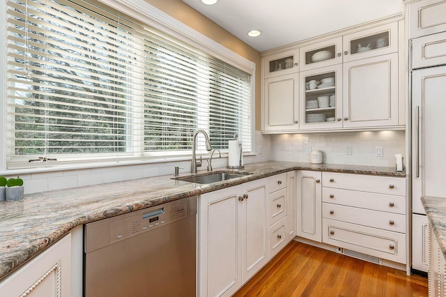 kitchen featuring light stone counters, a sink, light wood-style floors, tasteful backsplash, and stainless steel dishwasher