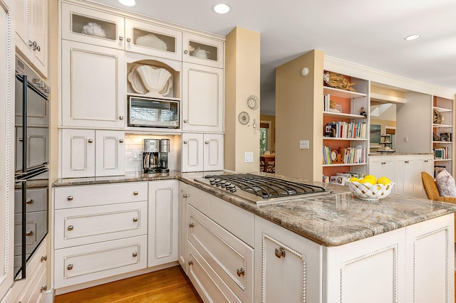 kitchen with light stone countertops, appliances with stainless steel finishes, a peninsula, recessed lighting, and glass insert cabinets