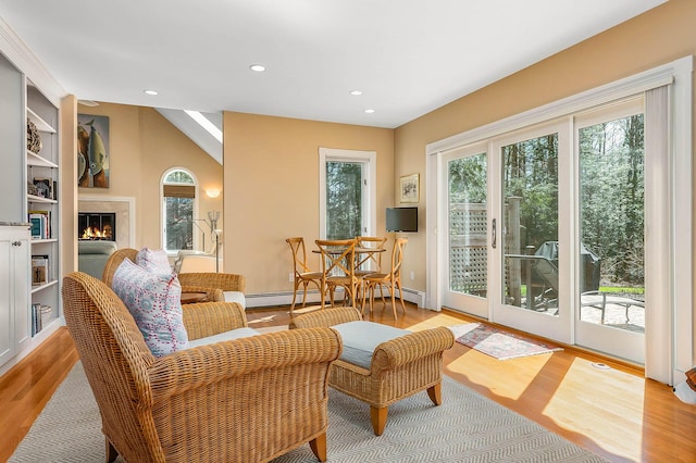 sitting room featuring recessed lighting, a warm lit fireplace, a wealth of natural light, and light wood-style flooring