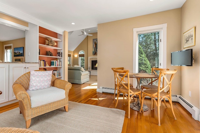 living area with ceiling fan, a warm lit fireplace, recessed lighting, a baseboard radiator, and light wood finished floors