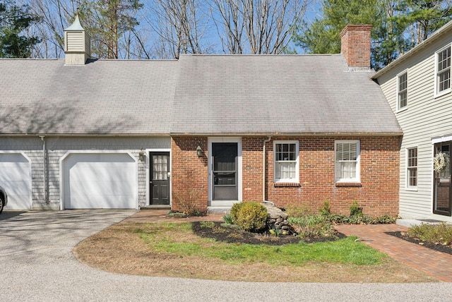 cape cod house with brick siding, an attached garage, a chimney, and aphalt driveway