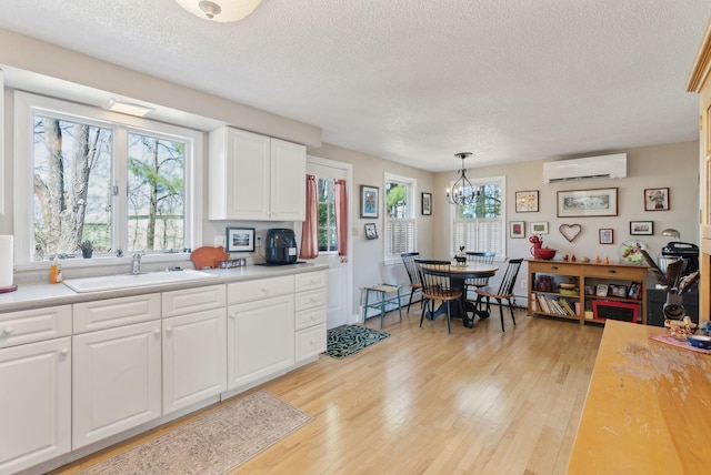 kitchen featuring a textured ceiling, a wall unit AC, a sink, and light wood-type flooring