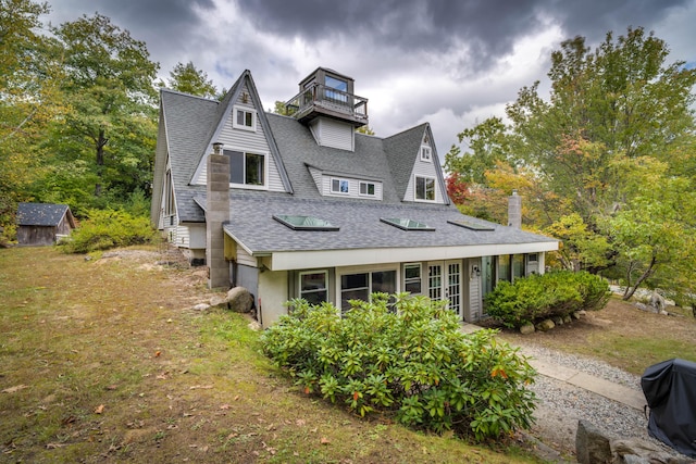 view of side of property with an outdoor structure, a shingled roof, a balcony, and a shed