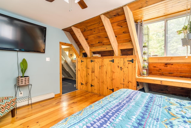 bedroom featuring wood-type flooring, wooden walls, baseboard heating, and vaulted ceiling