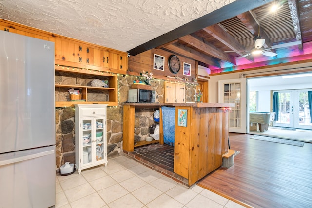kitchen with wooden walls, light tile patterned flooring, stainless steel appliances, a ceiling fan, and beamed ceiling