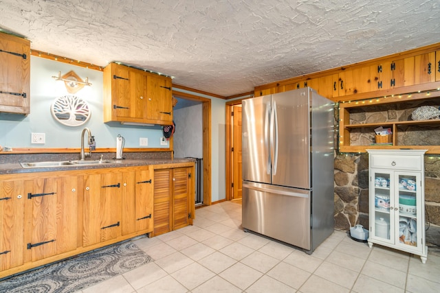 kitchen featuring brown cabinetry, dark countertops, a sink, freestanding refrigerator, and light tile patterned flooring