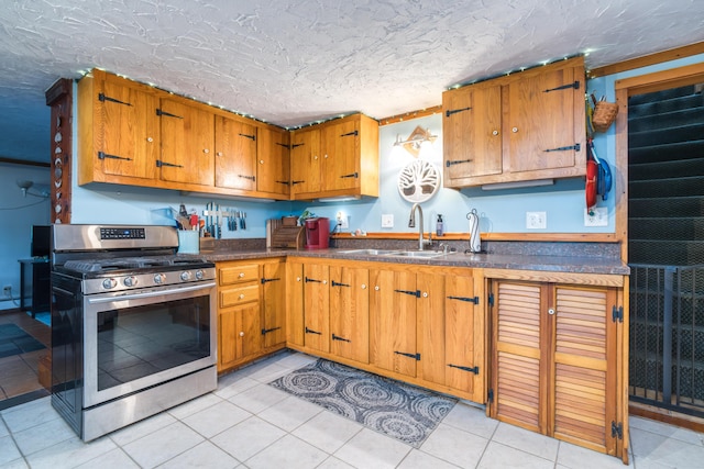 kitchen with brown cabinetry, dark countertops, a sink, light tile patterned floors, and gas stove