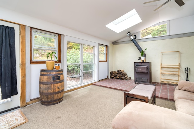 living area featuring a wood stove, carpet flooring, ceiling fan, and lofted ceiling with skylight
