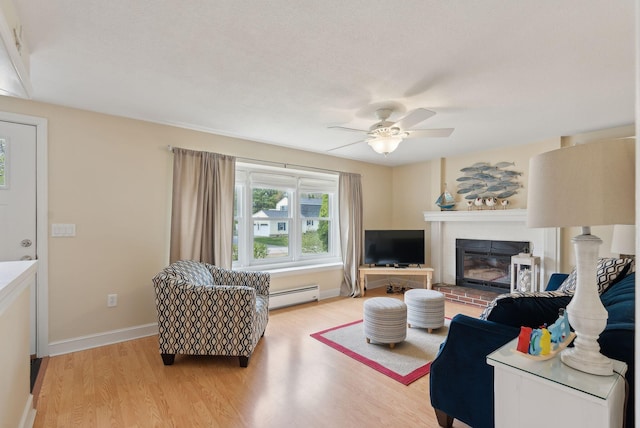 48 Woodside Dr, Kennebunk, ME 04043 - living area featuring a baseboard heating unit, light wood-type flooring, a ceiling fan, a brick fireplace, and baseboards