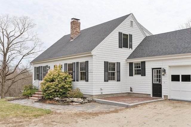 exterior space with a shingled roof, a chimney, and an attached garage