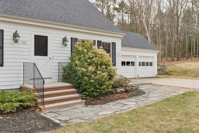 exterior space with a garage, a shingled roof, and driveway