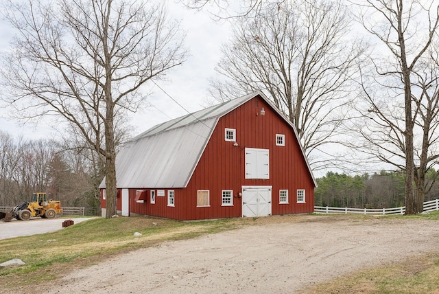 view of barn featuring dirt driveway and fence
