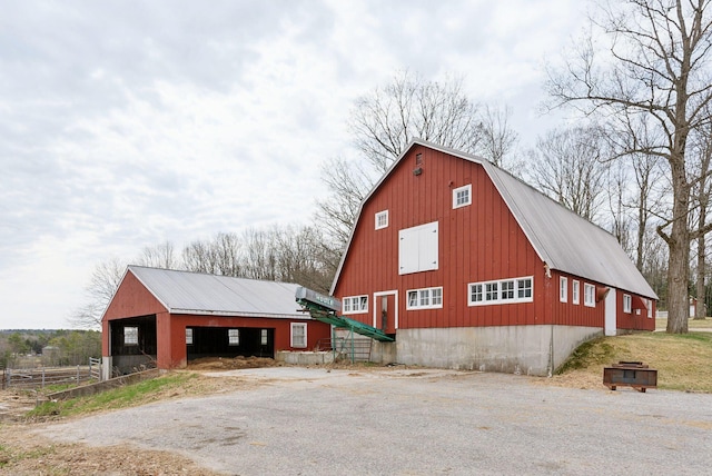 exterior space with a barn, a gambrel roof, aphalt driveway, an outbuilding, and metal roof