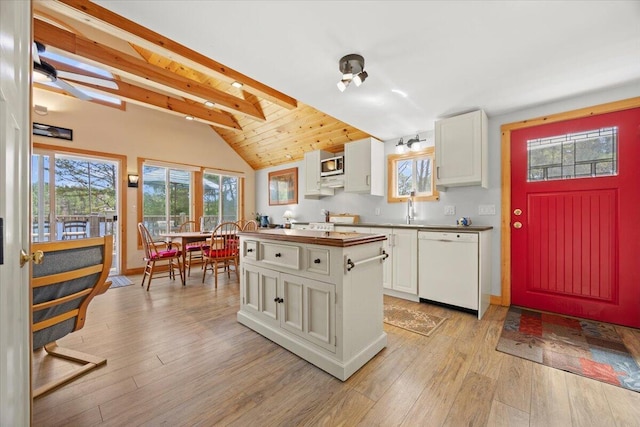 kitchen with white dishwasher, vaulted ceiling with beams, white cabinetry, stainless steel microwave, and light wood finished floors