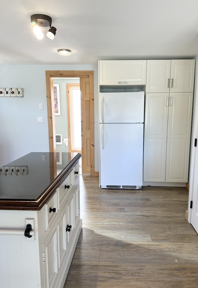 kitchen featuring dark countertops, freestanding refrigerator, white cabinetry, light wood-type flooring, and visible vents